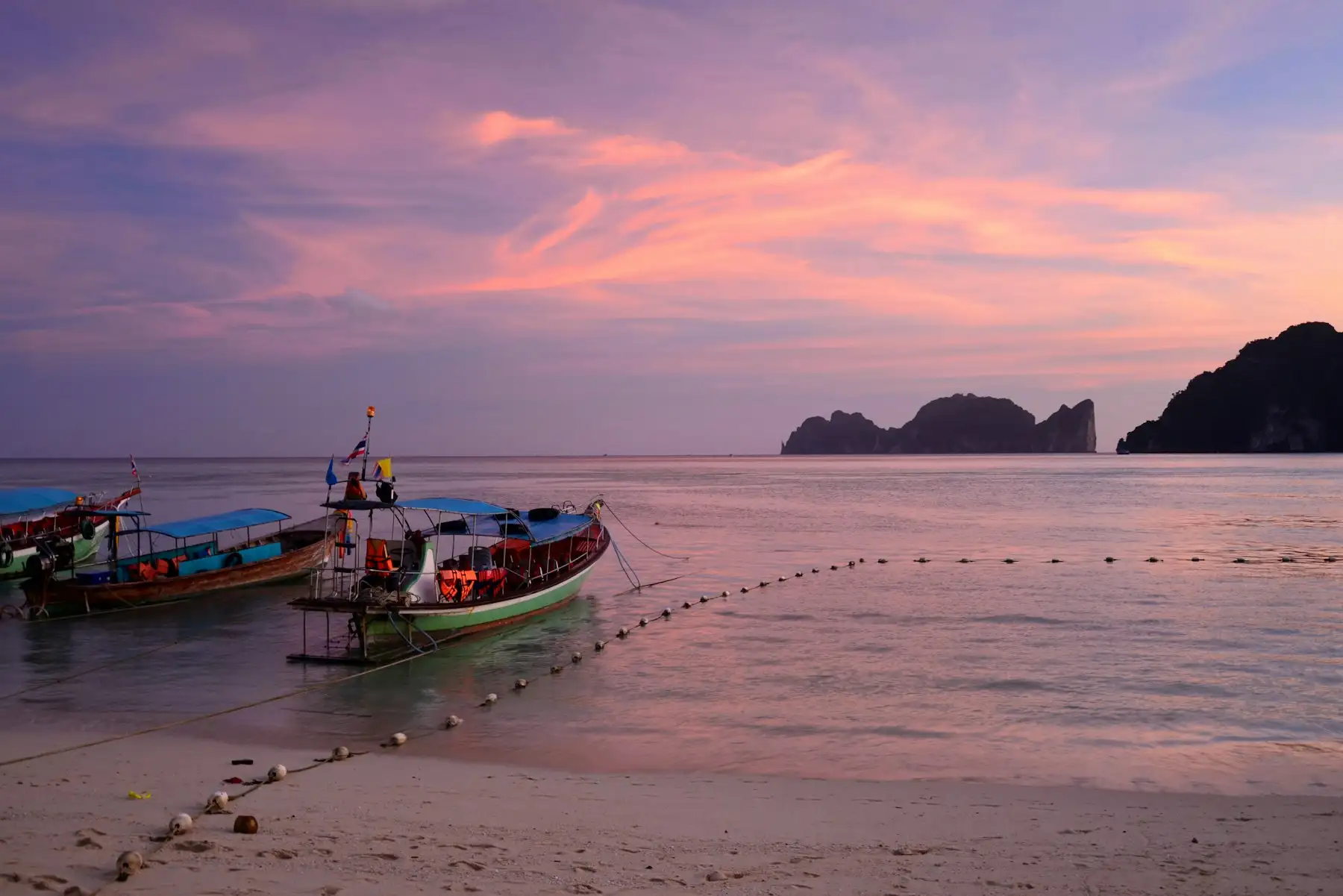 Wooden longtail boats moored near the shore under a pink sunset sky