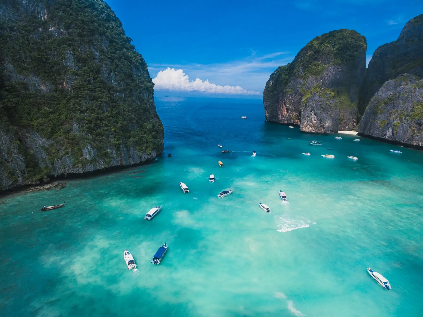 Small boats on the turquoise water of Maya Bay between steep limestone cliffs