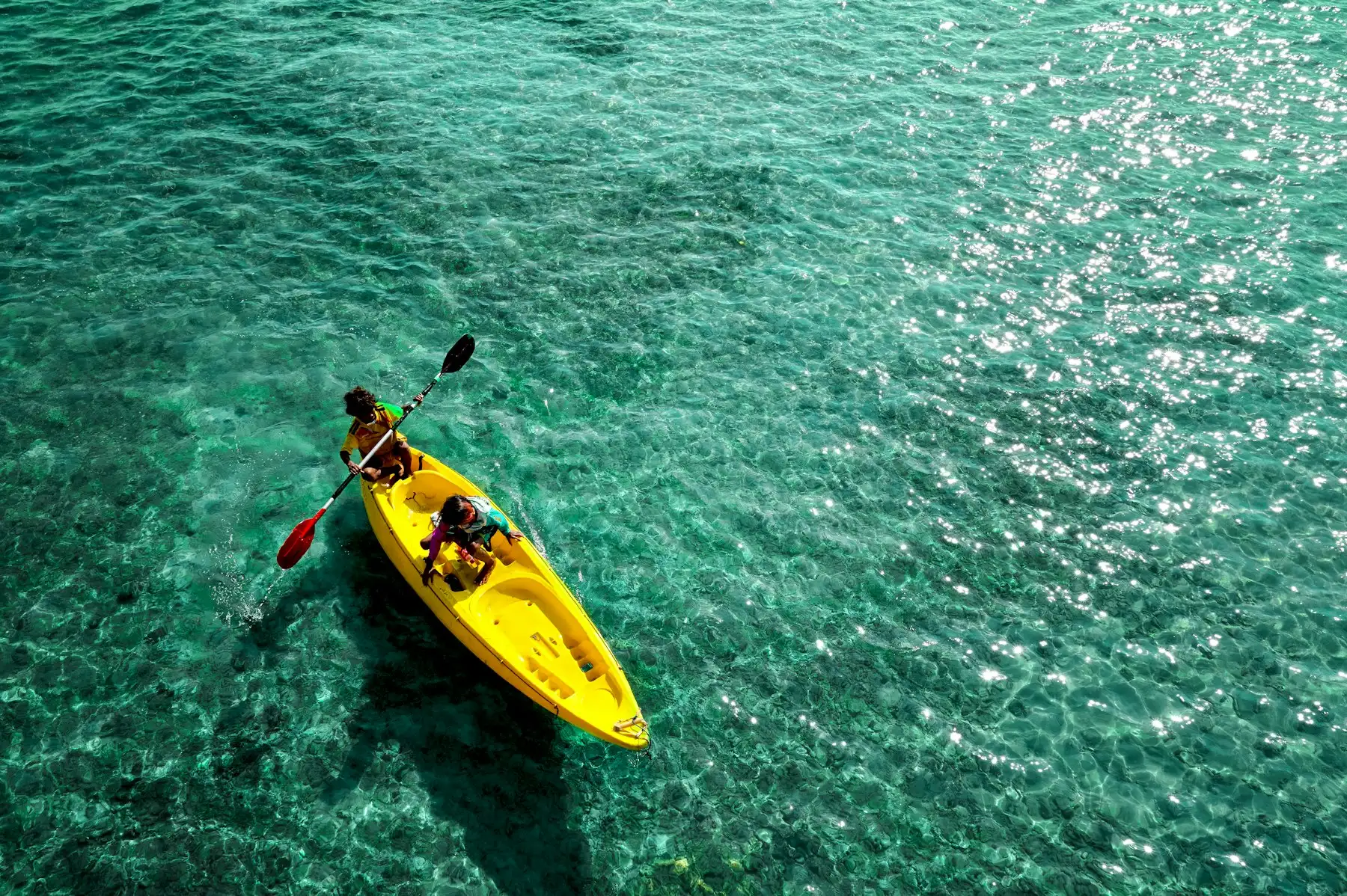 A yellow sea kayak on clear turquoise water seen from above